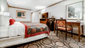 A hotel room with a bed, a desk, a chair, a dresser, a mirror, and a large window.