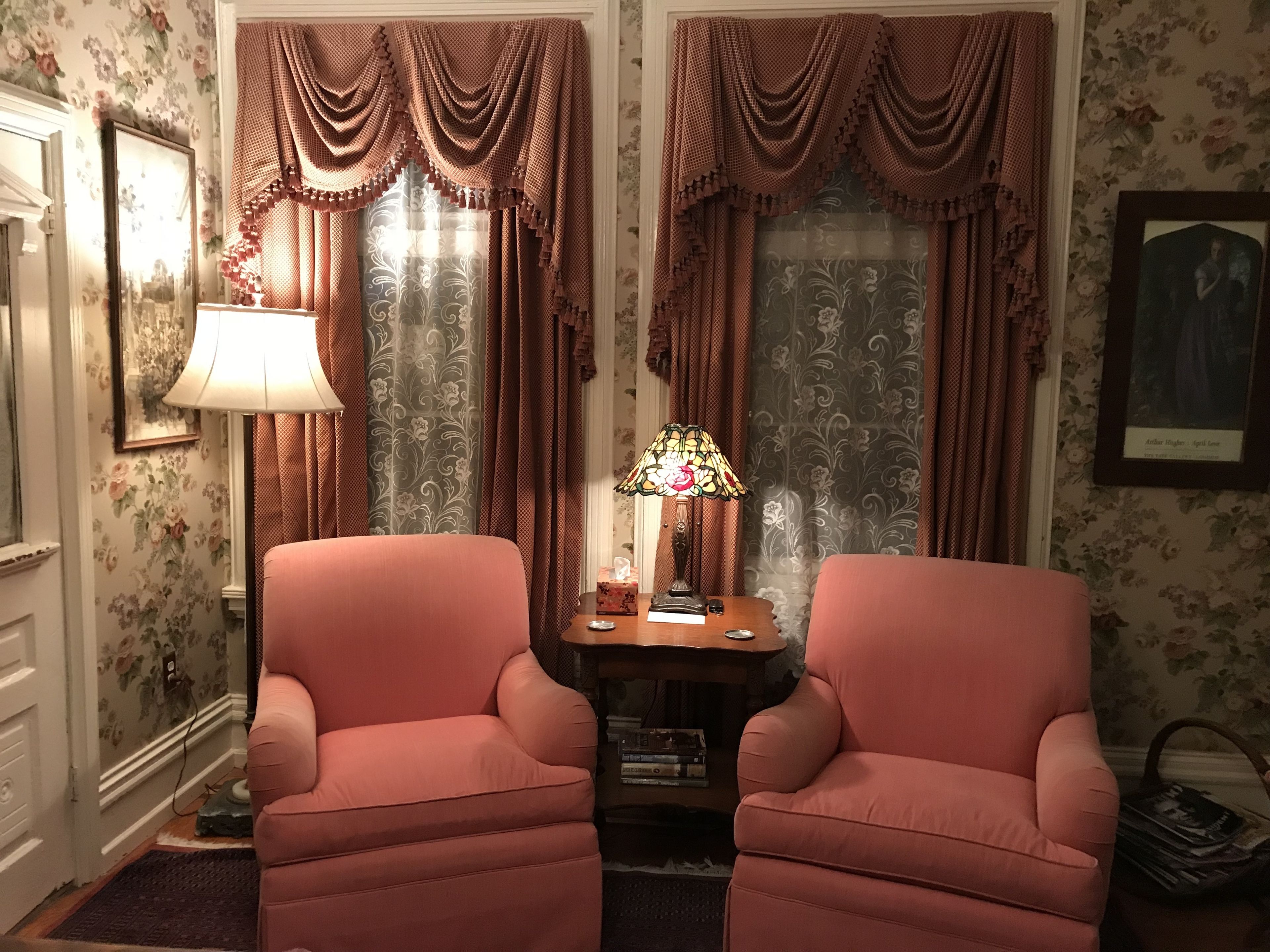 Quarto com duas poltronas cor-de-rosa, uma mesinha com abajur e papel de parede floral.