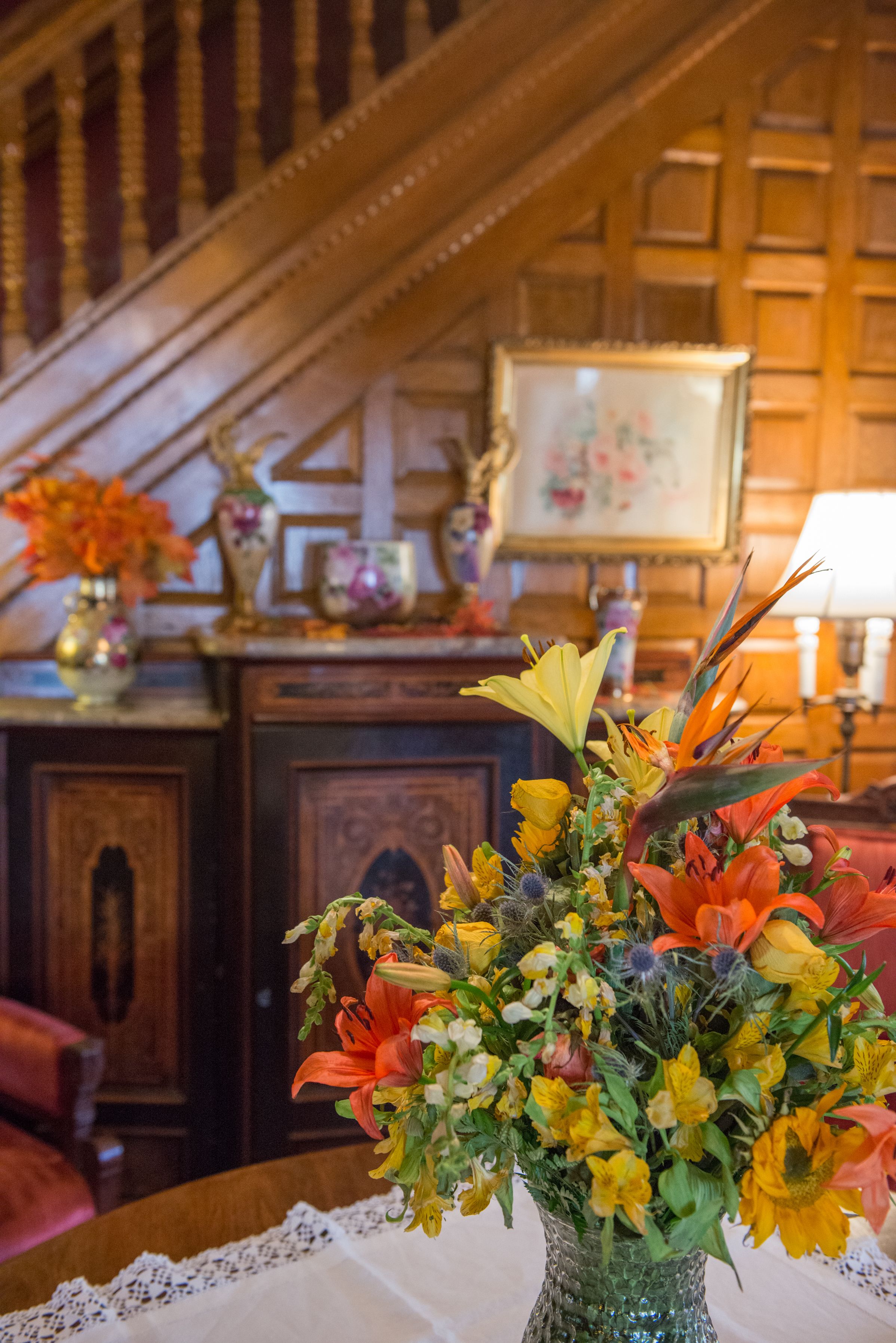 A room with a wooden staircase, a wooden cabinet, and a table with a floral arrangement.