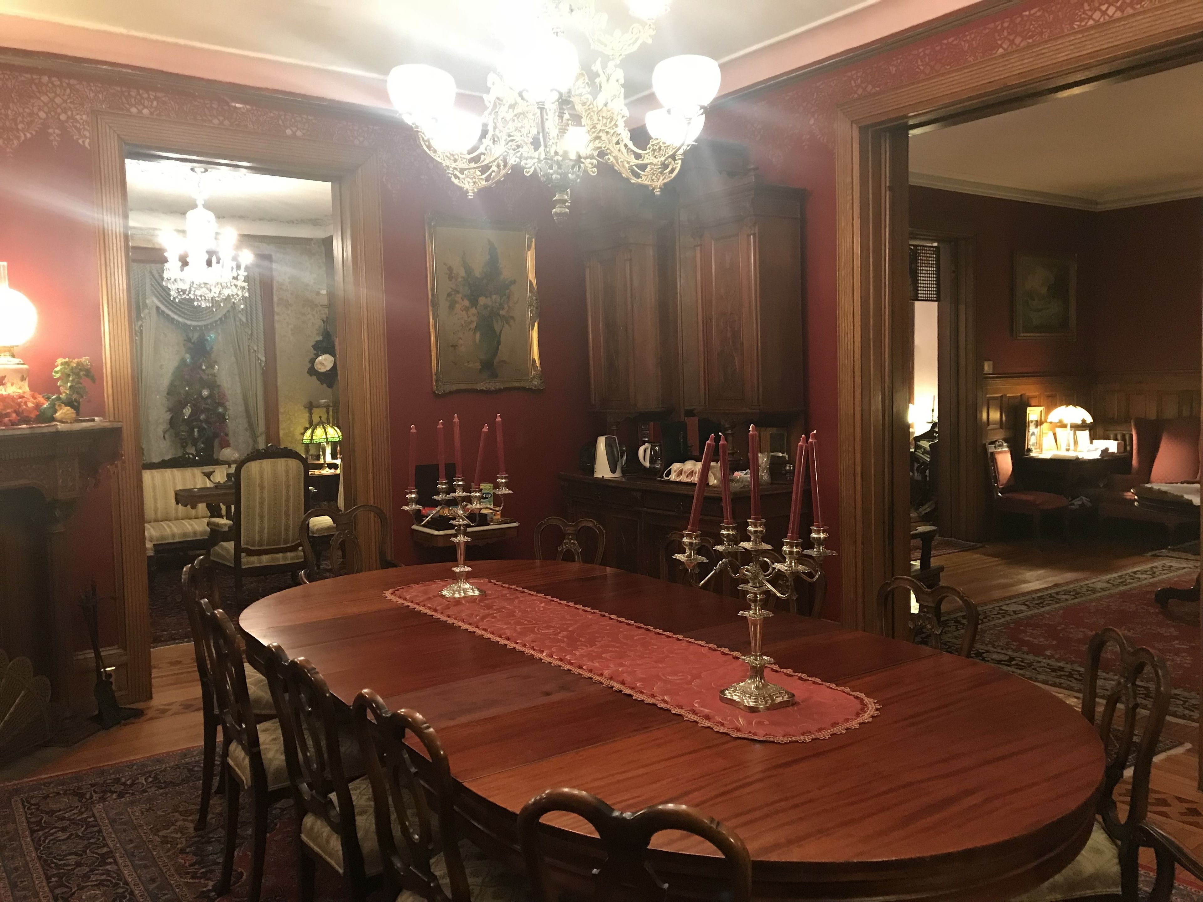 A formal dining room with a wooden table, chairs, a chandelier, and a red carpet.