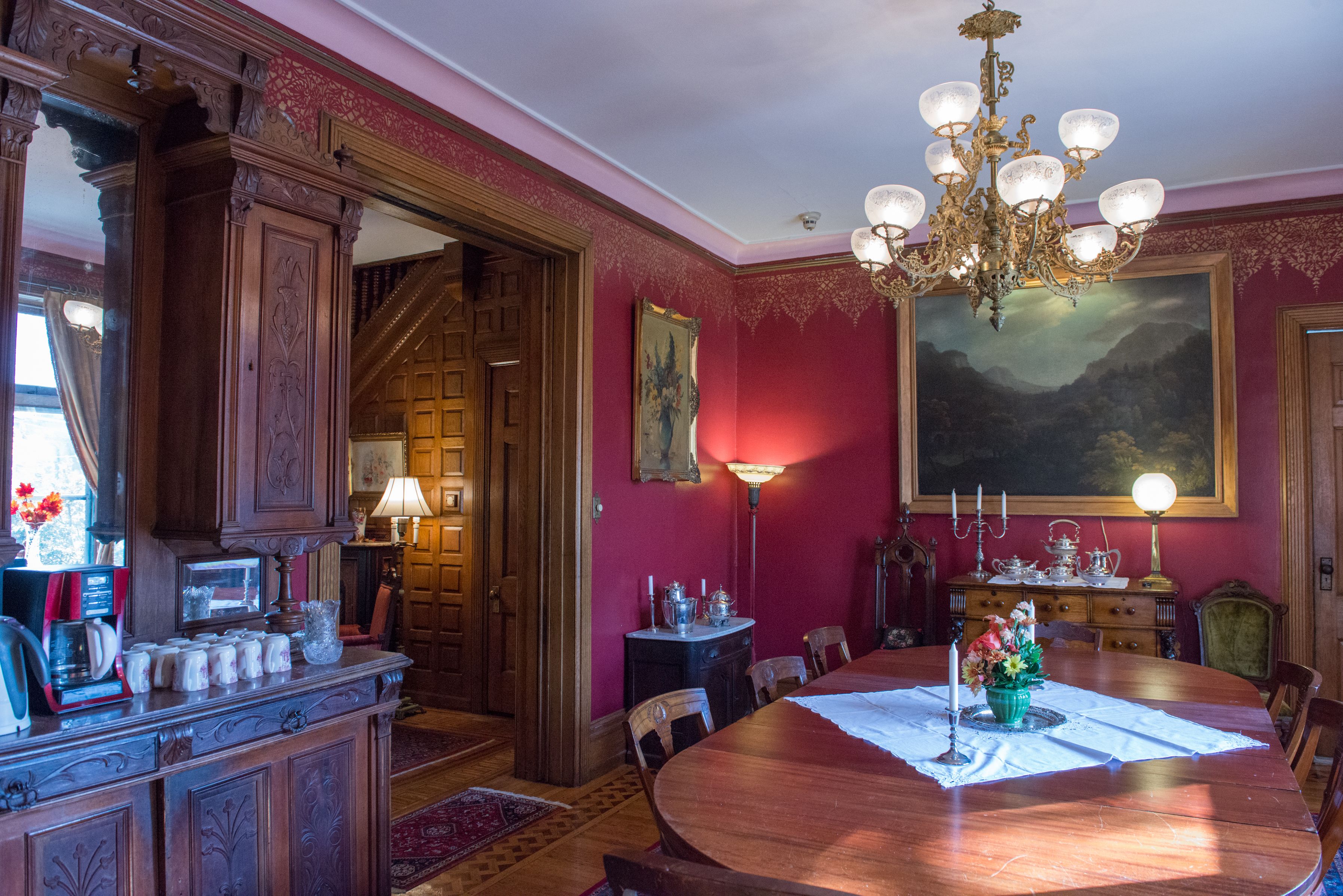 A dining room with a large wooden table, a chandelier, and a painting on the wall.