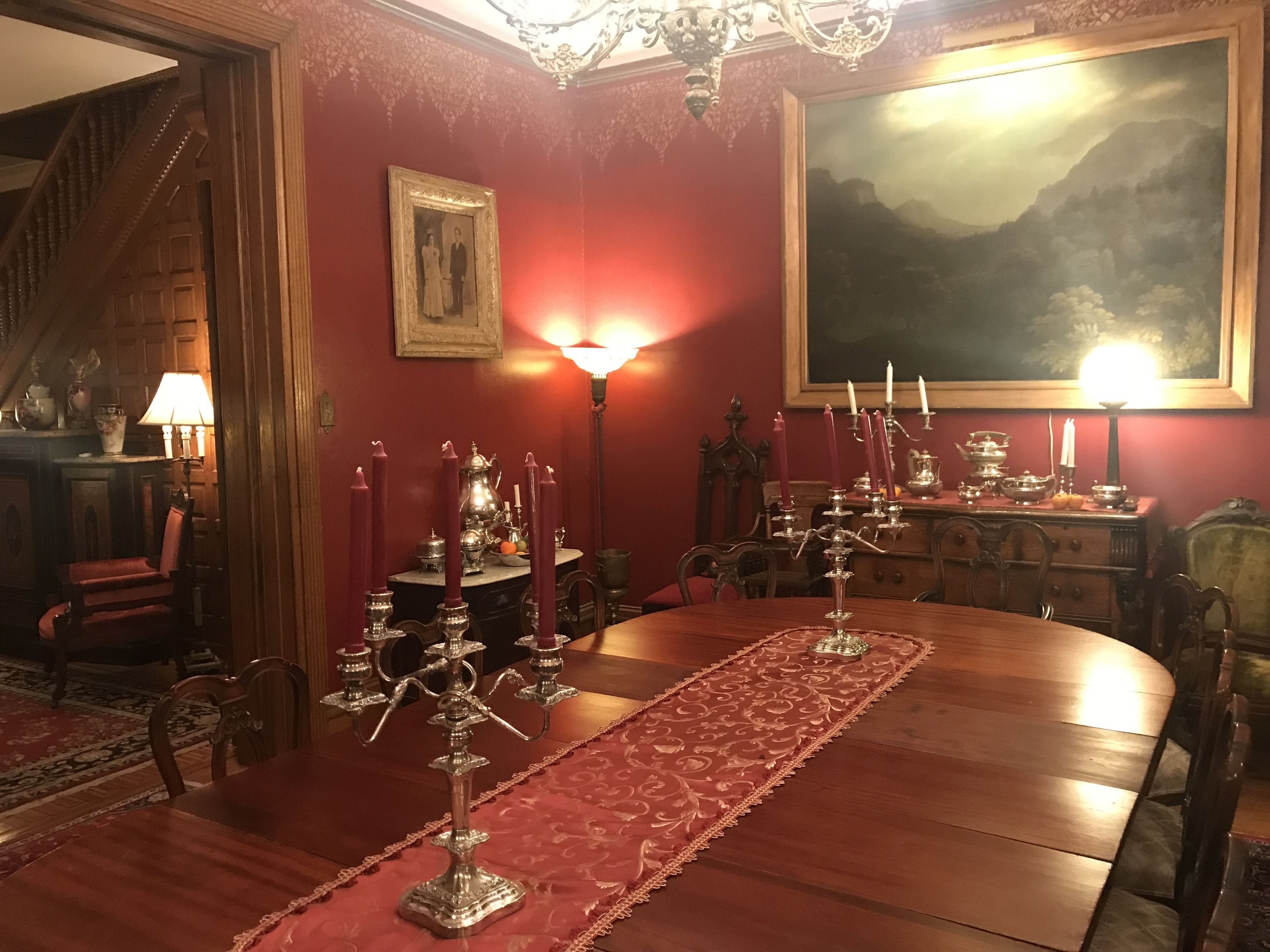 A formal dining room with a wooden table, red carpet, and candle holders.