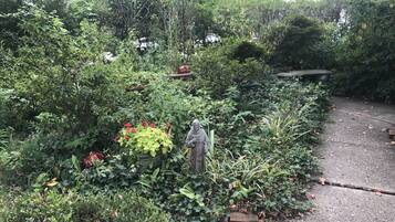 Un jardin avec un feuillage dense, une statue et un chemin en béton.