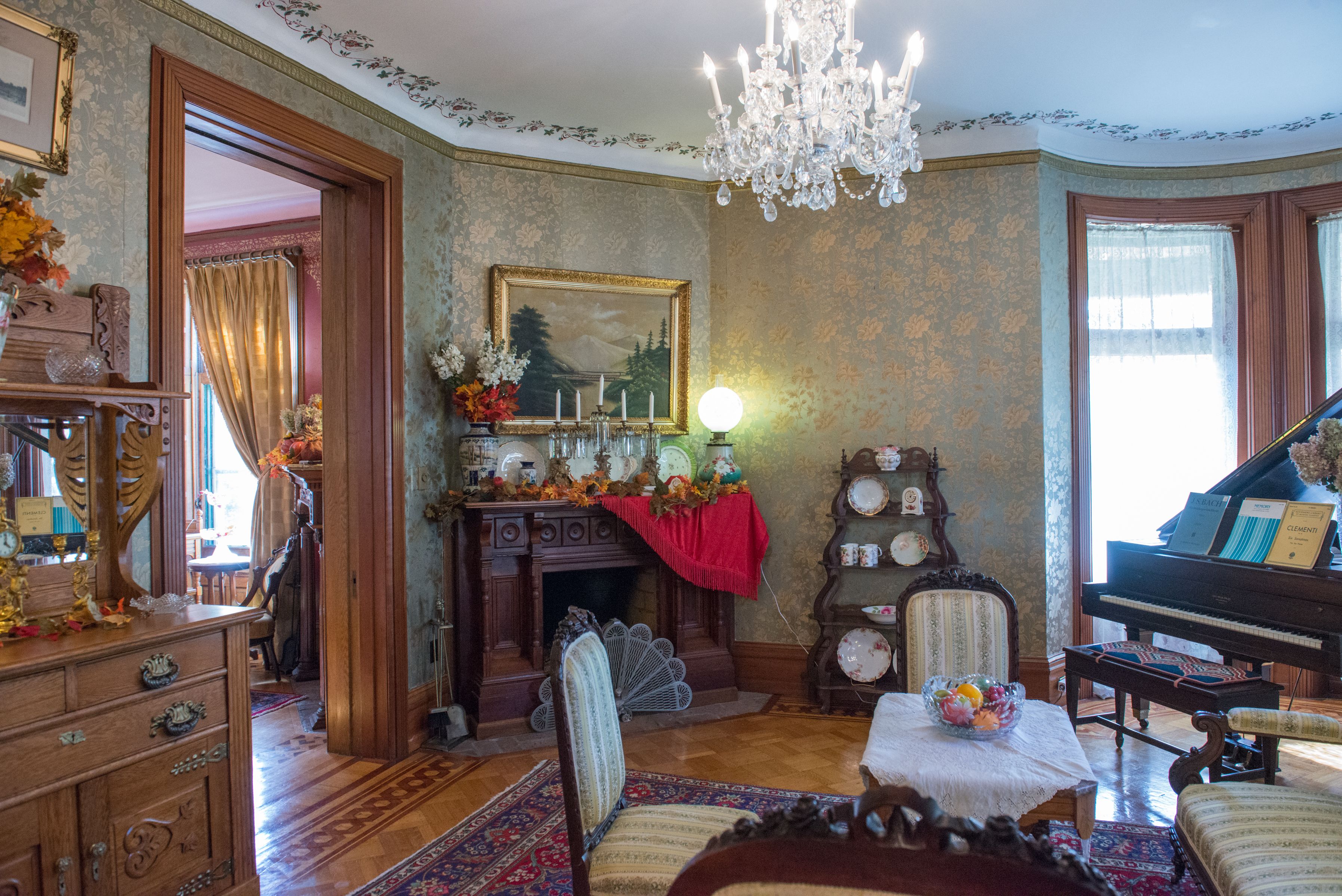 Uma sala ampla com um piano, lareira e um candelabro.