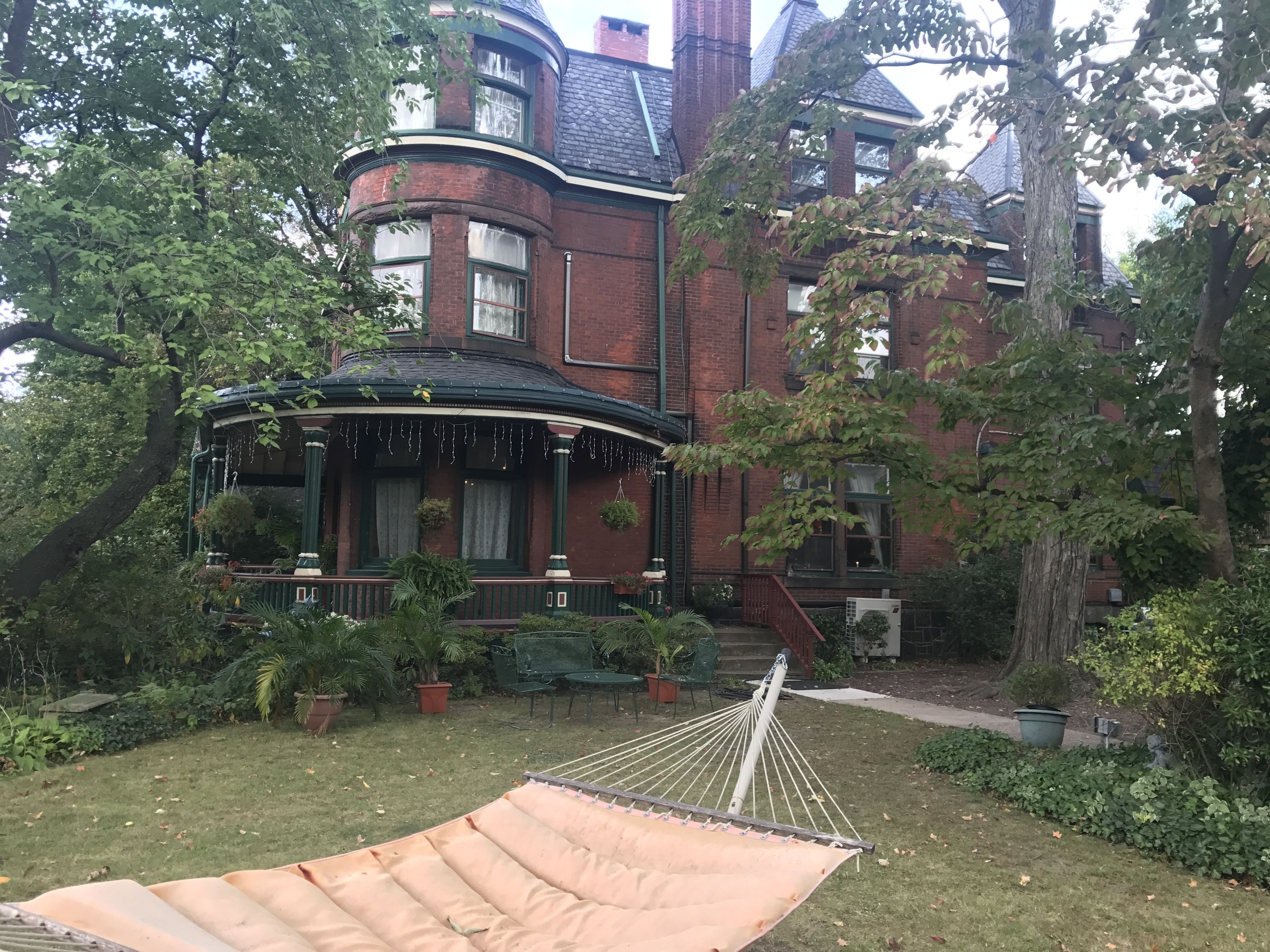 Una casa de estilo victoriano con ventanal semicircular, un porche amueblado y una hamaca en el jardín.