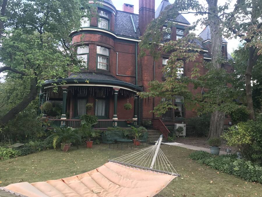 Una casa de estilo victoriano con ventanal semicircular, un porche amueblado y una hamaca en el jardín.