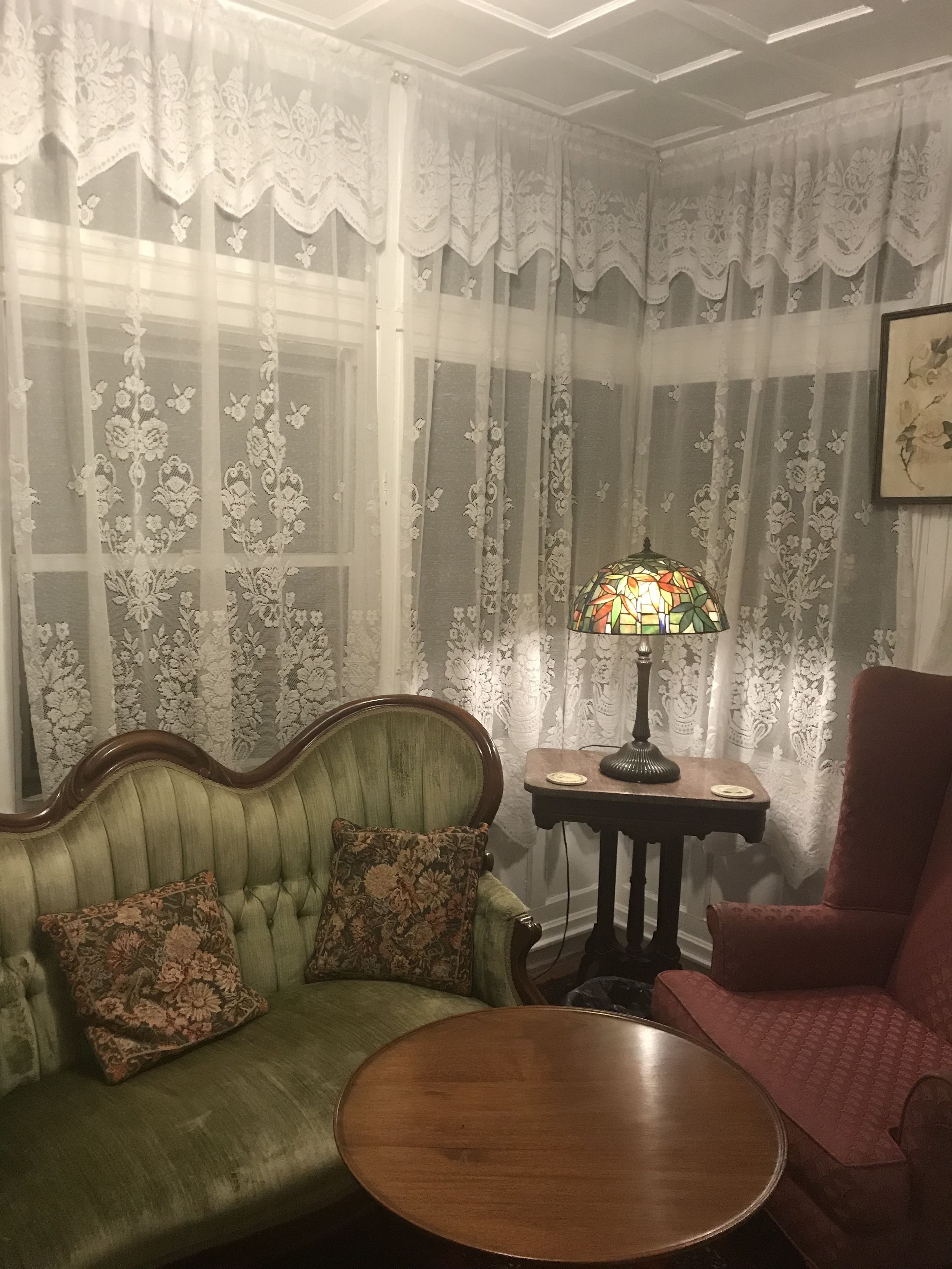 A room with a green upholstered sofa, a red armchair, a round wooden coffee table, and a stained glass lamp.