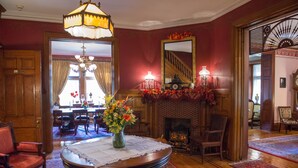Une pièce au décor traditionnel, avec une cheminée, un coin repas à l’arrière-plan et une table ronde recouverte d’une nappe en dentelle.
