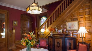 Une grande pièce avec un escalier, des boiseries, un lustre et un arrangement floral sur une table.