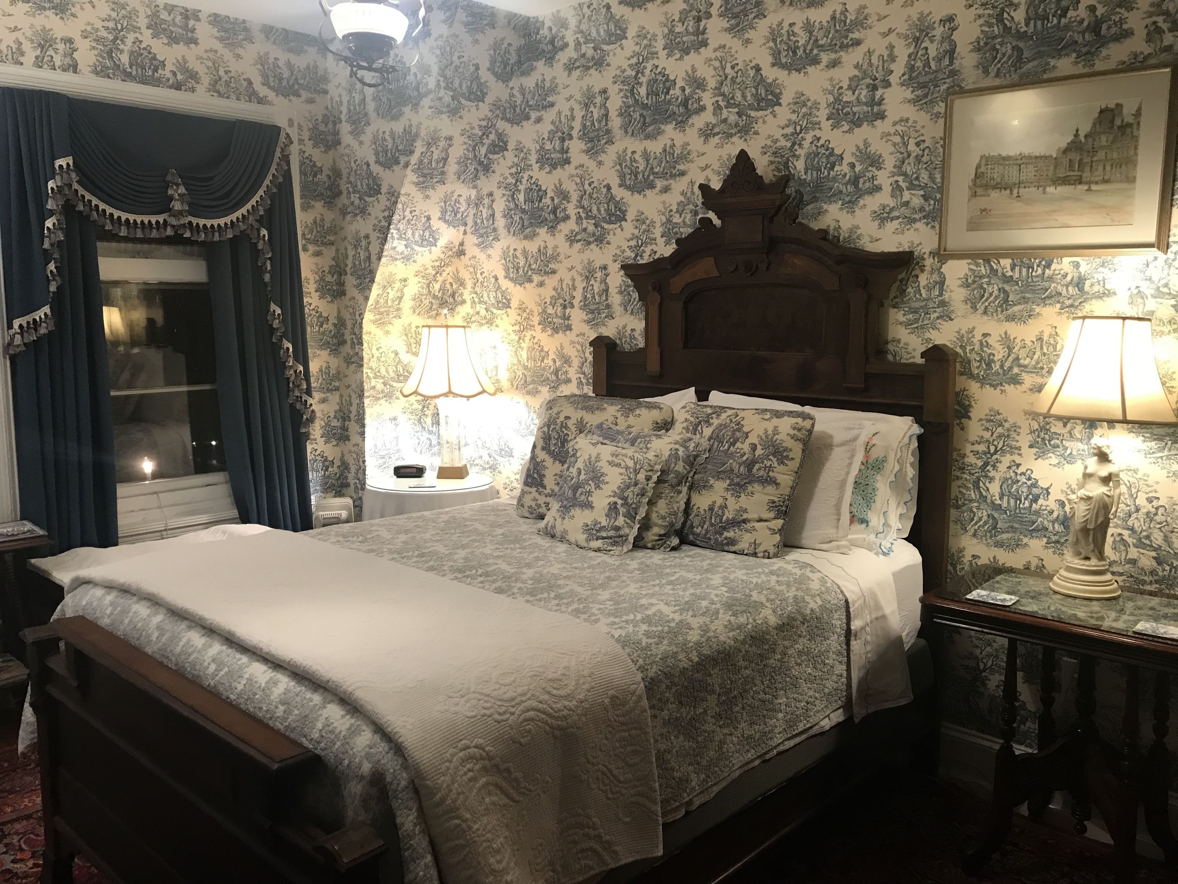 Un dormitorio tradicional con cama de madera, papel tapiz floral y decoración clásica.