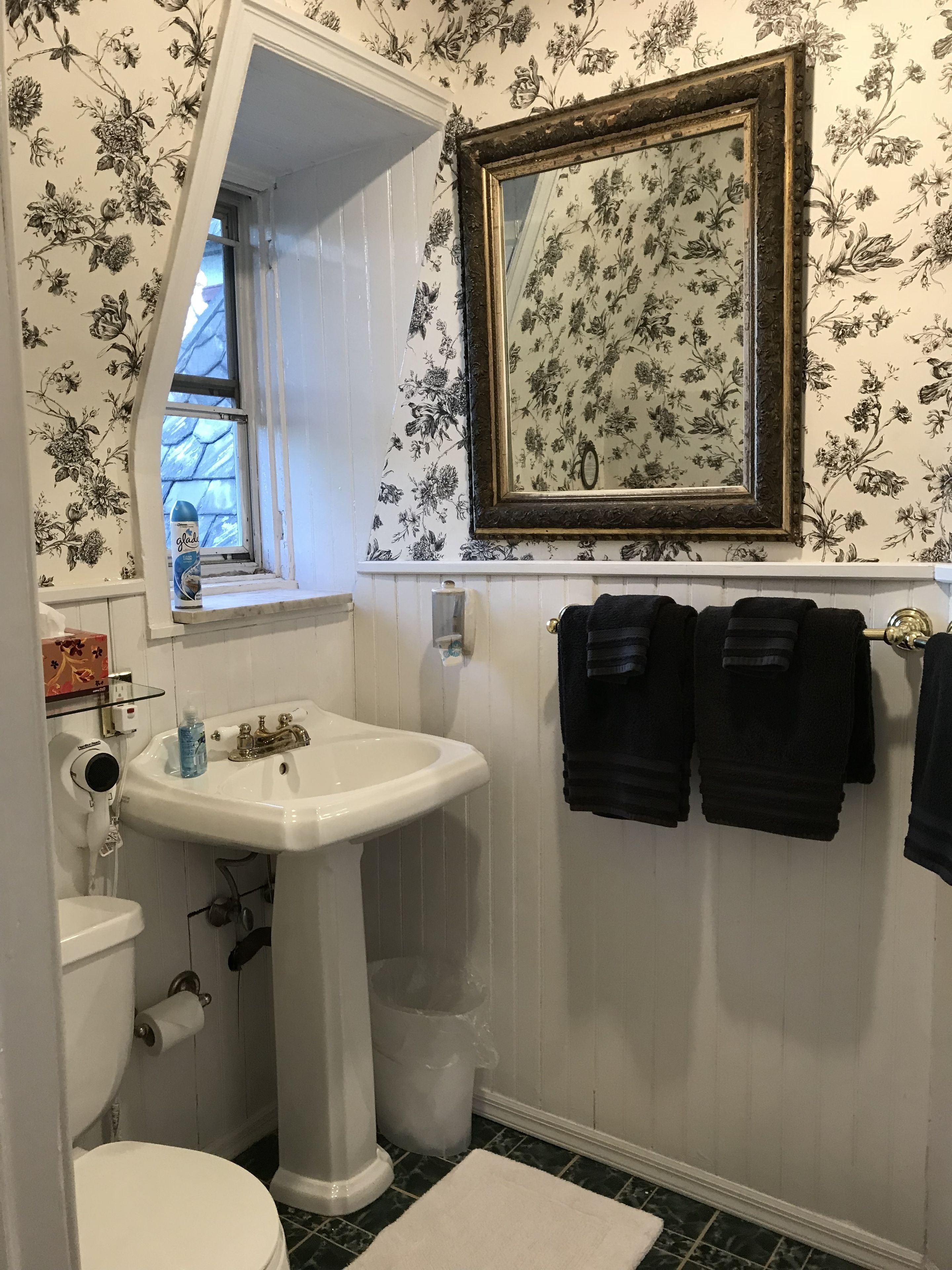 A bathroom with a white sink, a toilet, a window, and a mirror with a floral wallpaper.
