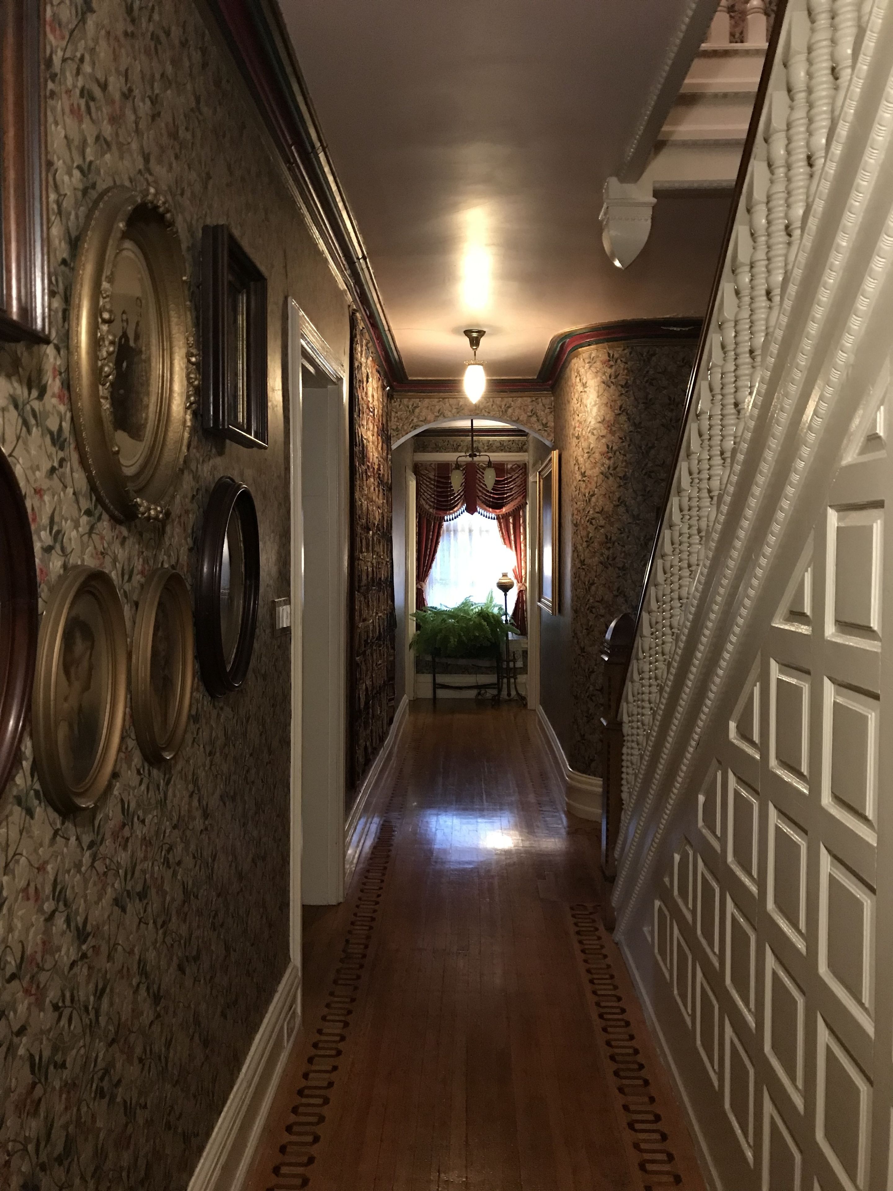 A hallway with patterned wallpaper, a wooden floor, and a staircase with a decorative railing.