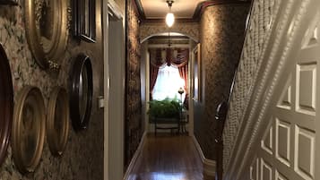 A hallway with patterned wallpaper, a wooden floor, and a staircase with a decorative railing.