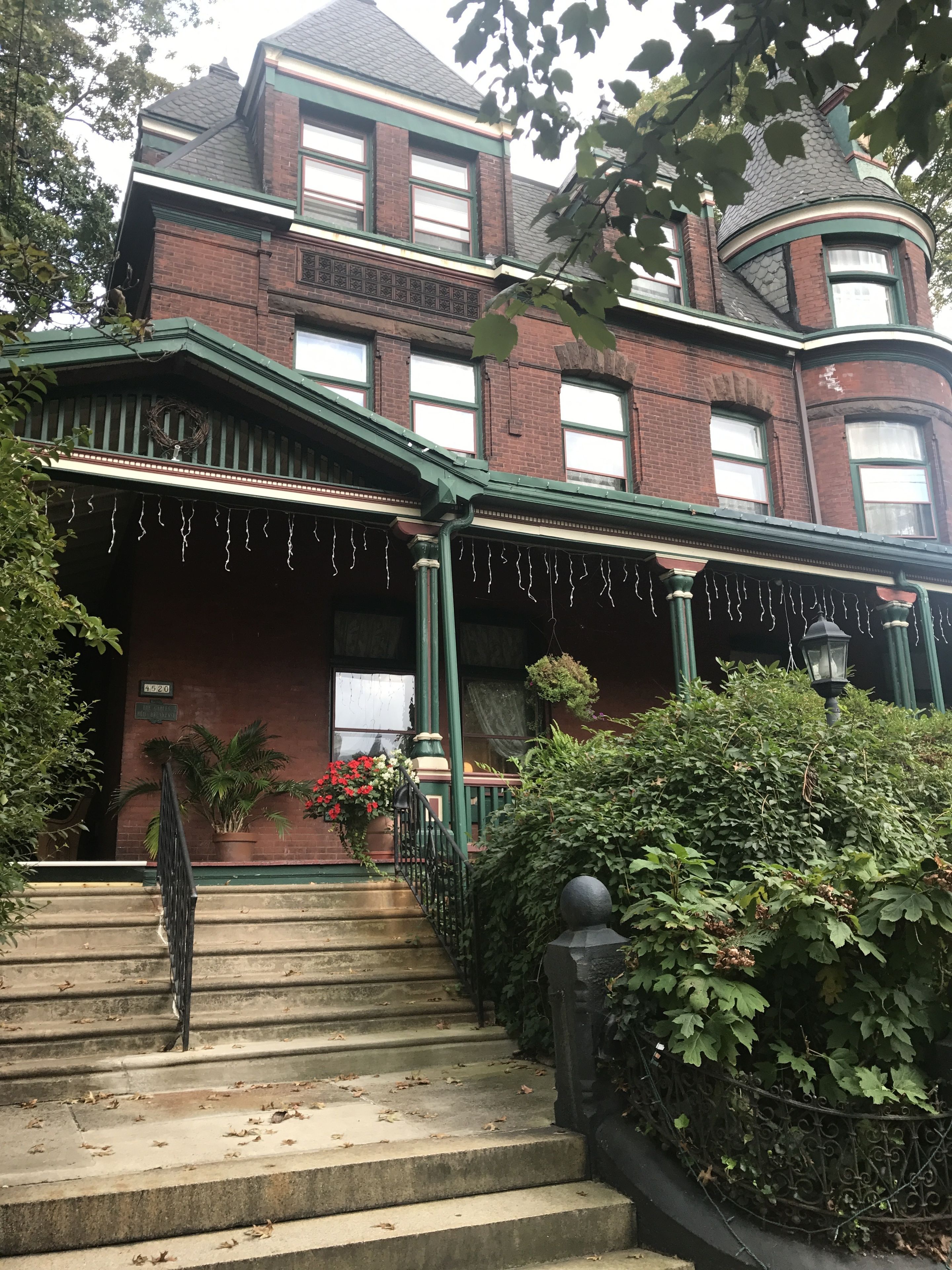 A Victorian-style house with a wrap-around porch, brick facade, and a turret.