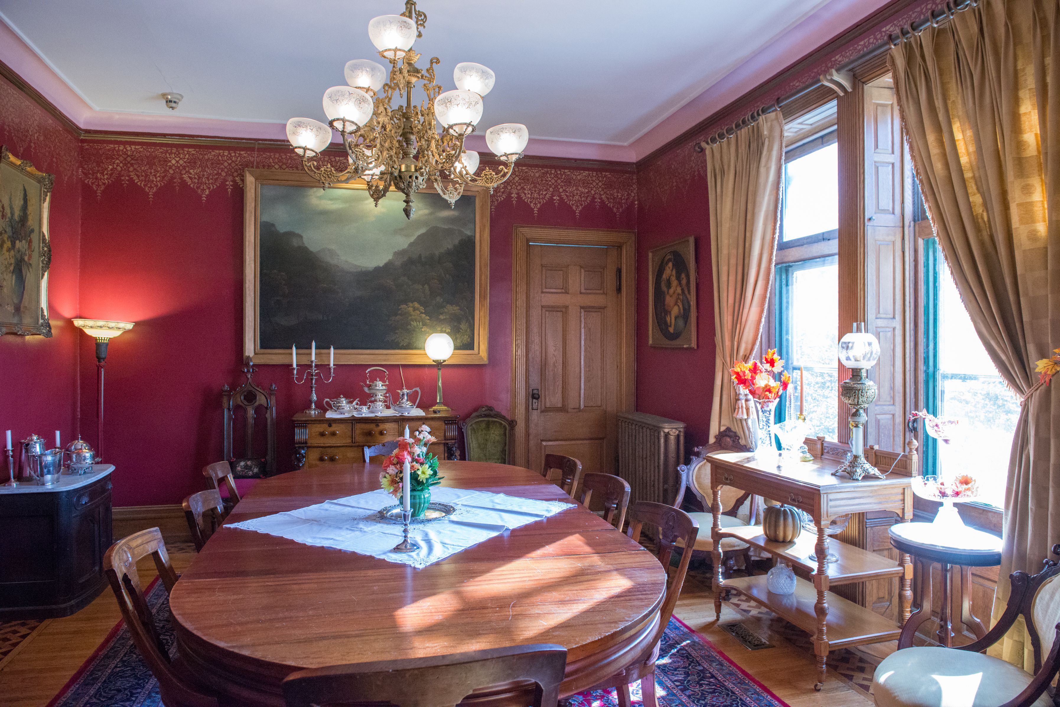 Ein Esszimmer mit einem großen Holztisch, Stühlen, einer Kronleuchter und Blick ins Freie durch ein Fenster.