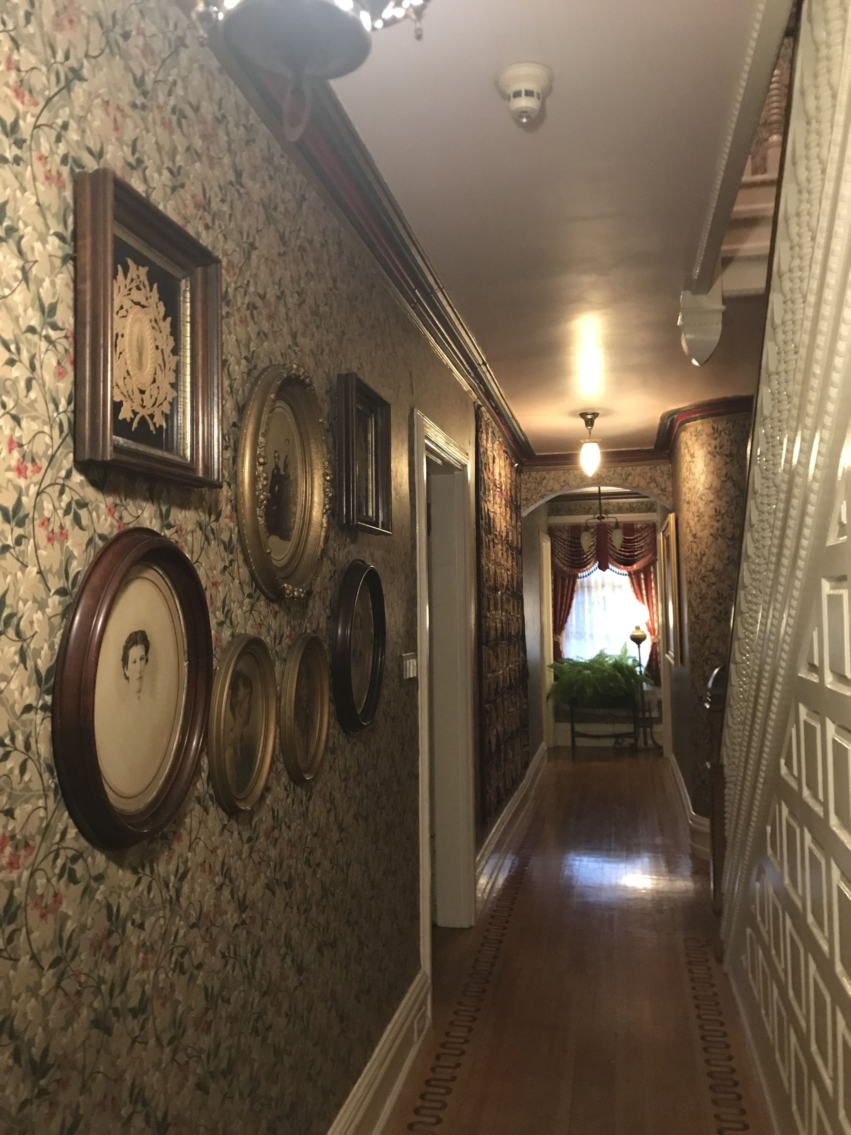 A hallway with floral wallpaper, multiple framed mirrors, and a chandelier.