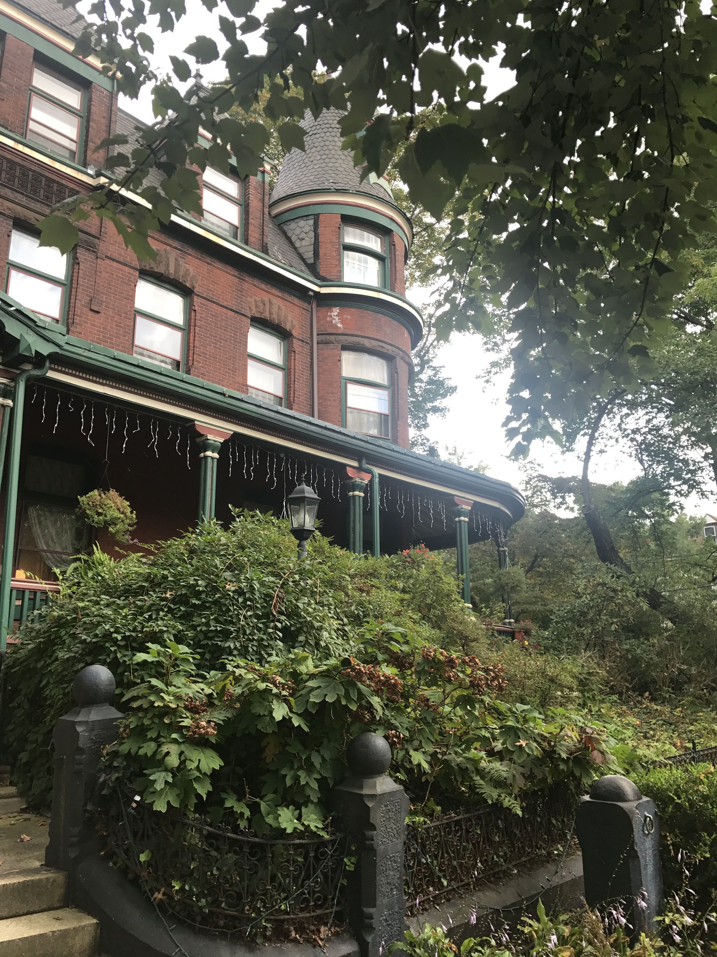 A historic building with a turret, ivy-covered walls, and a covered front porch with string lights.