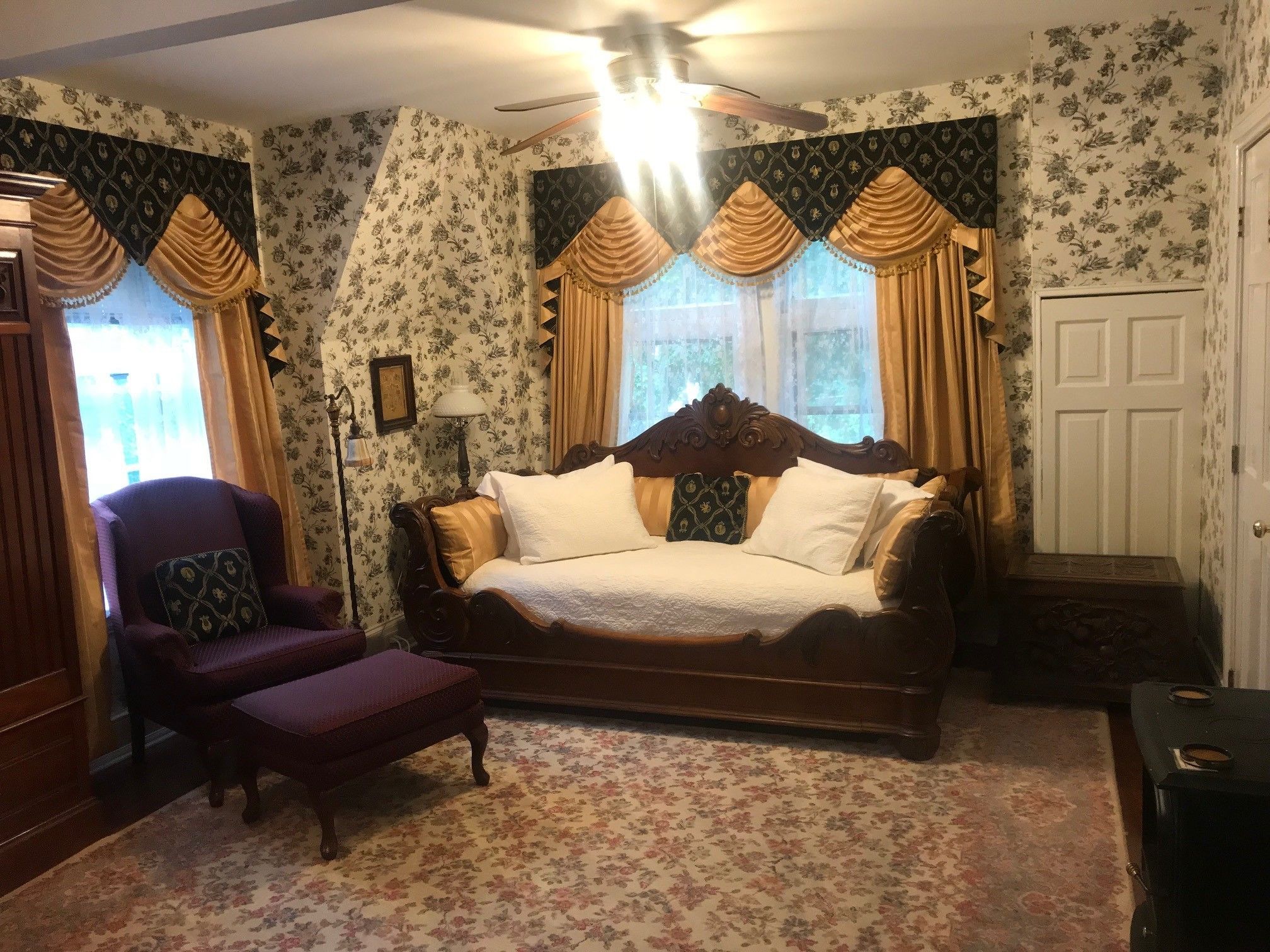 A bedroom with a wooden bed, floral wallpaper, and a chair.