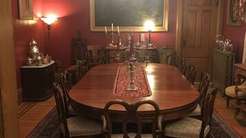 Uma sala de jantar formal com uma grande mesa de madeira, cadeiras ornamentadas, um candelabro e uma pintura de paisagem na parede.
