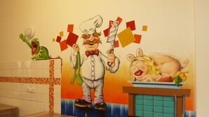 A kitchen with a tiled backsplash, a wooden countertop, and a wall mural featuring cartoon characters. - HappyGoLucky Hotel & Hostel (Berlin)