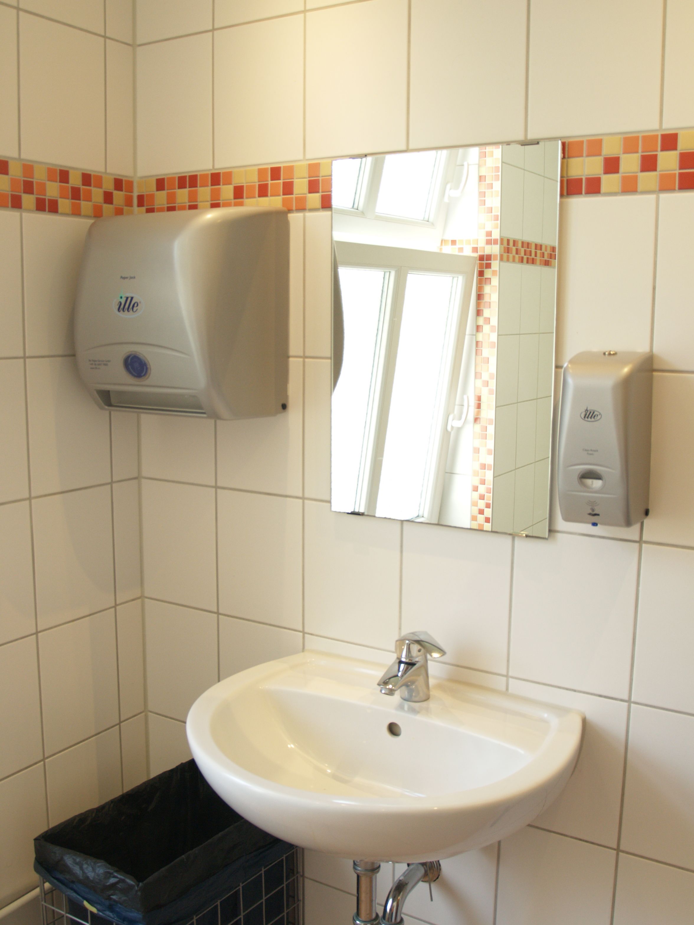 A bathroom with a white sink, a mirror, and two paper towel dispensers.