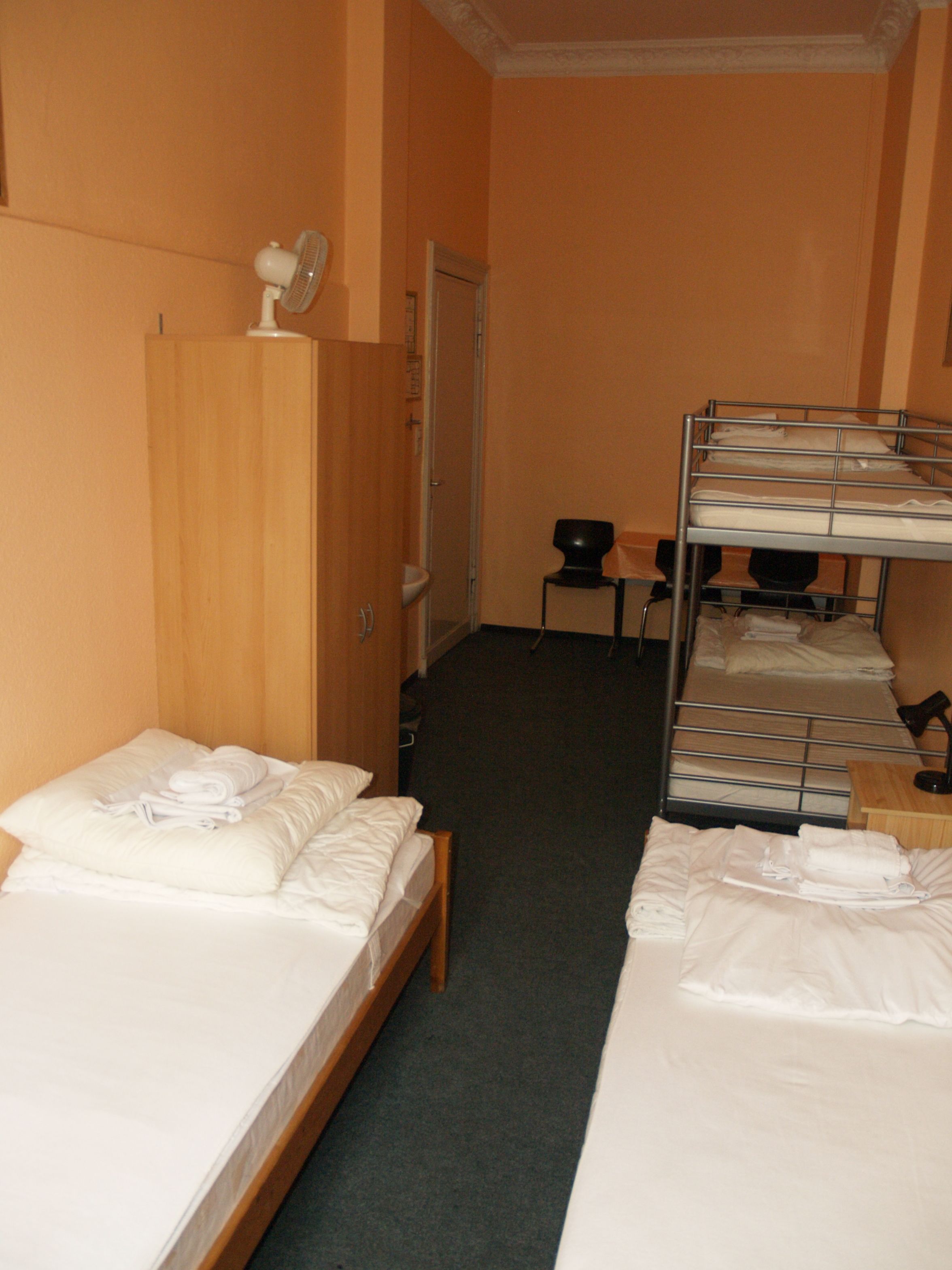 A hotel room with two single beds, a wooden wardrobe, a desk with a chair, and a bunk bed.
