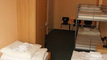 A hotel room with two single beds, a wooden wardrobe, a desk with a chair, and a bunk bed.