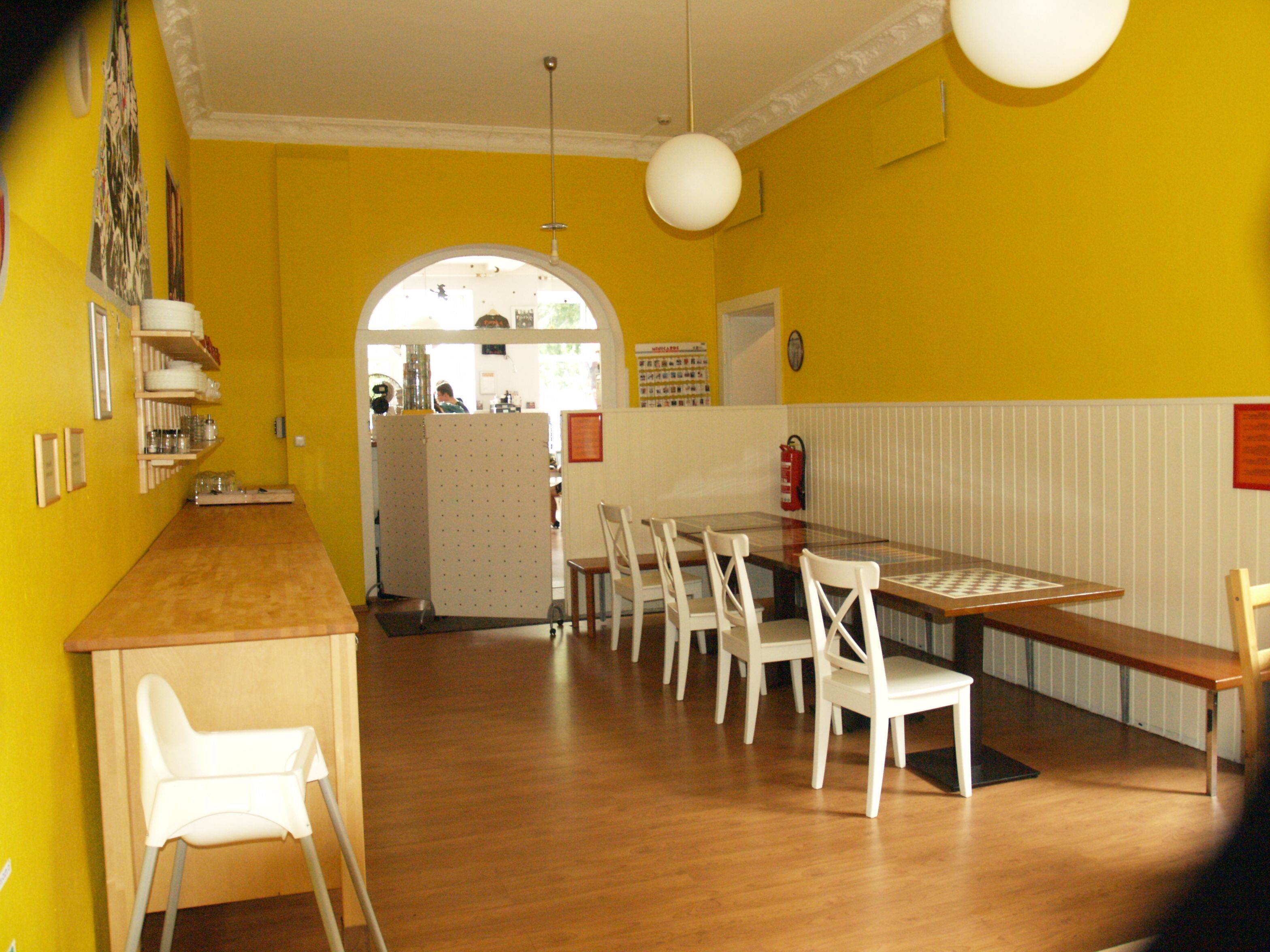 Un comedor con mesa de madera y sillas blancas, paredes amarillas y techo blanco.