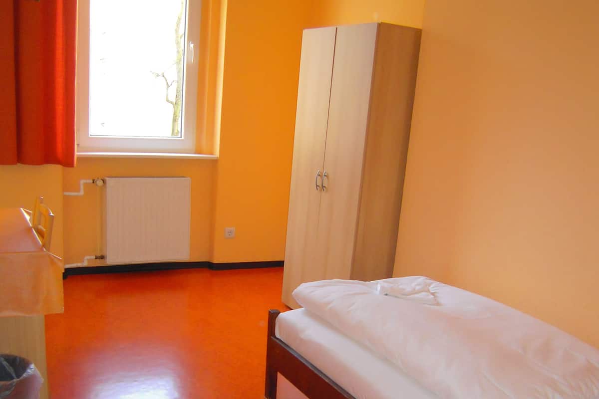 A room with a bed, a wardrobe, a radiator, and a window with curtains.