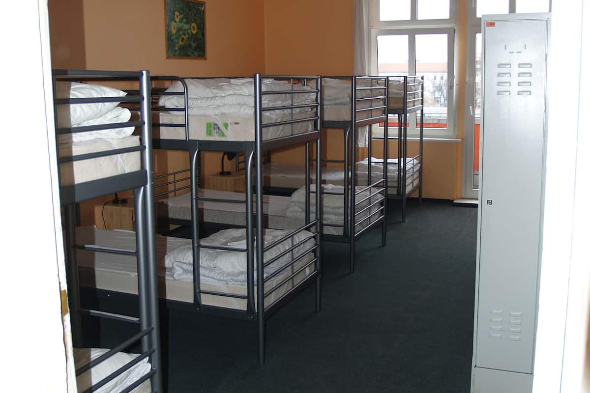 A dormitory room with bunk beds, a window with curtains, and a metal locker.