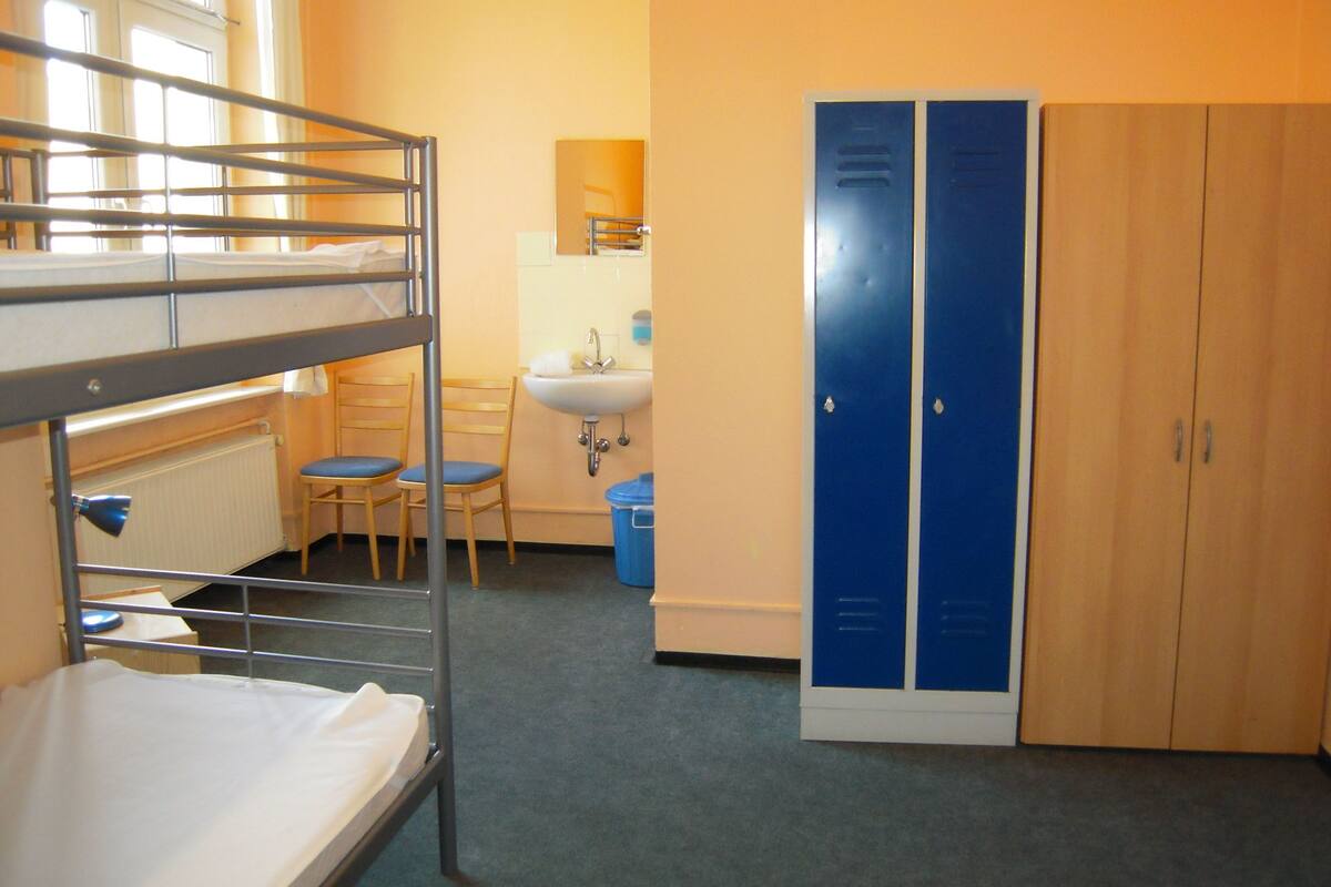 A dormitory room with bunk beds, a sink, a mirror, and a wardrobe.