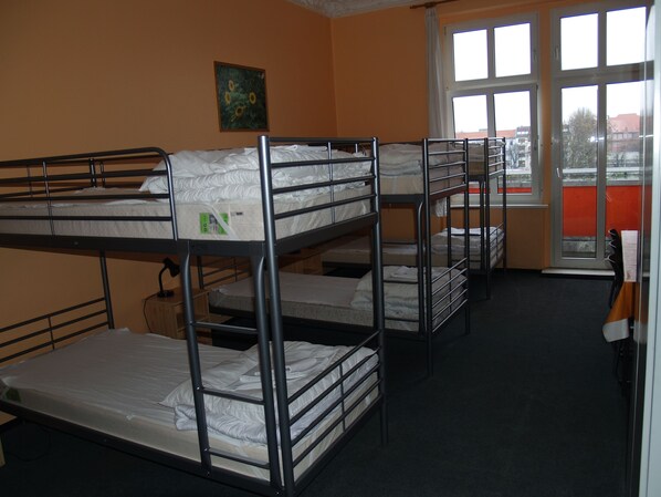 A dormitory room with bunk beds, a painting on the wall, and a window with a view of buildings outside.