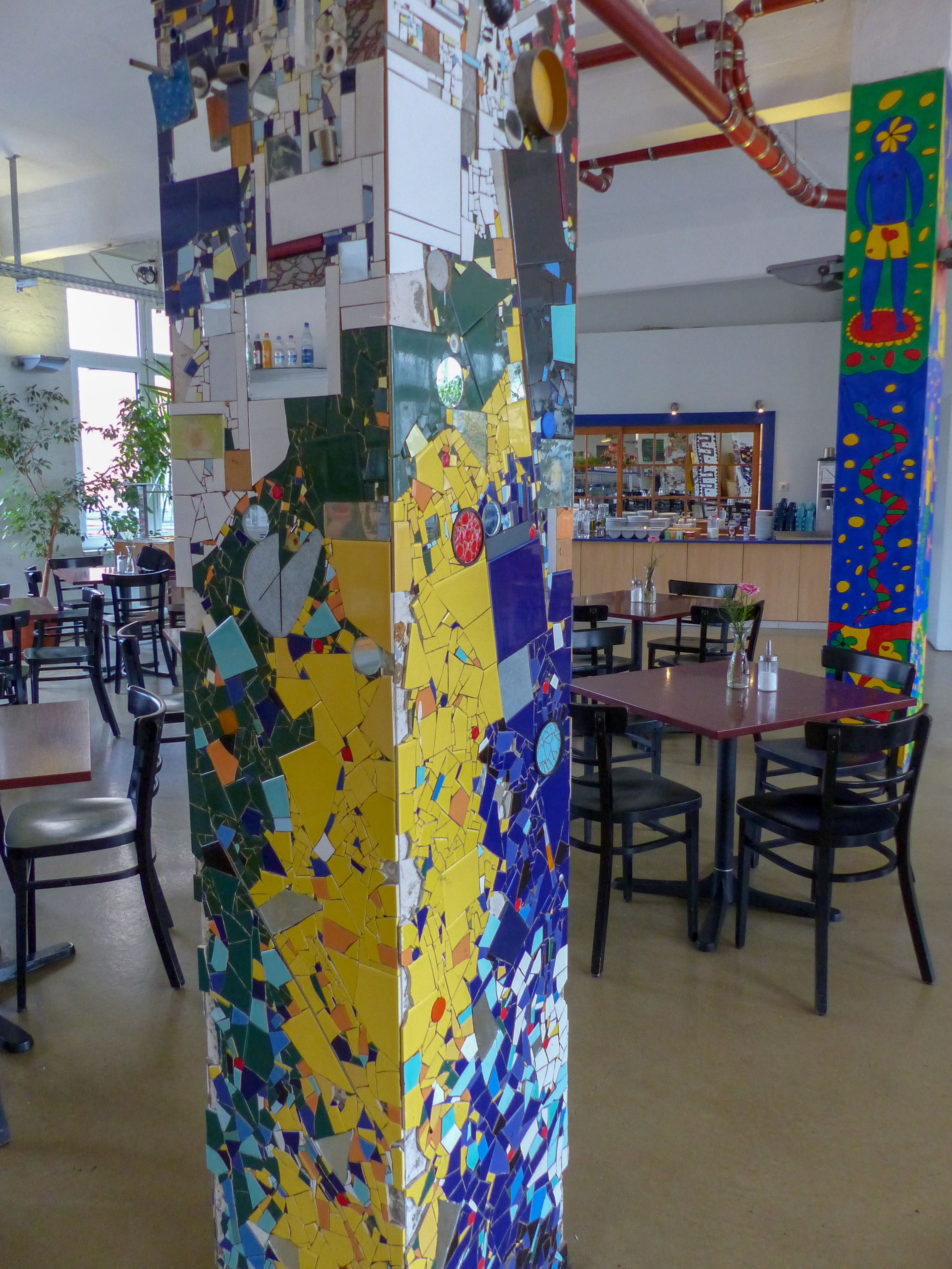 Un espace repas agrémenté d’un mur en mosaïque, de tables, de chaises et d’un comptoir où sont exposés divers articles.