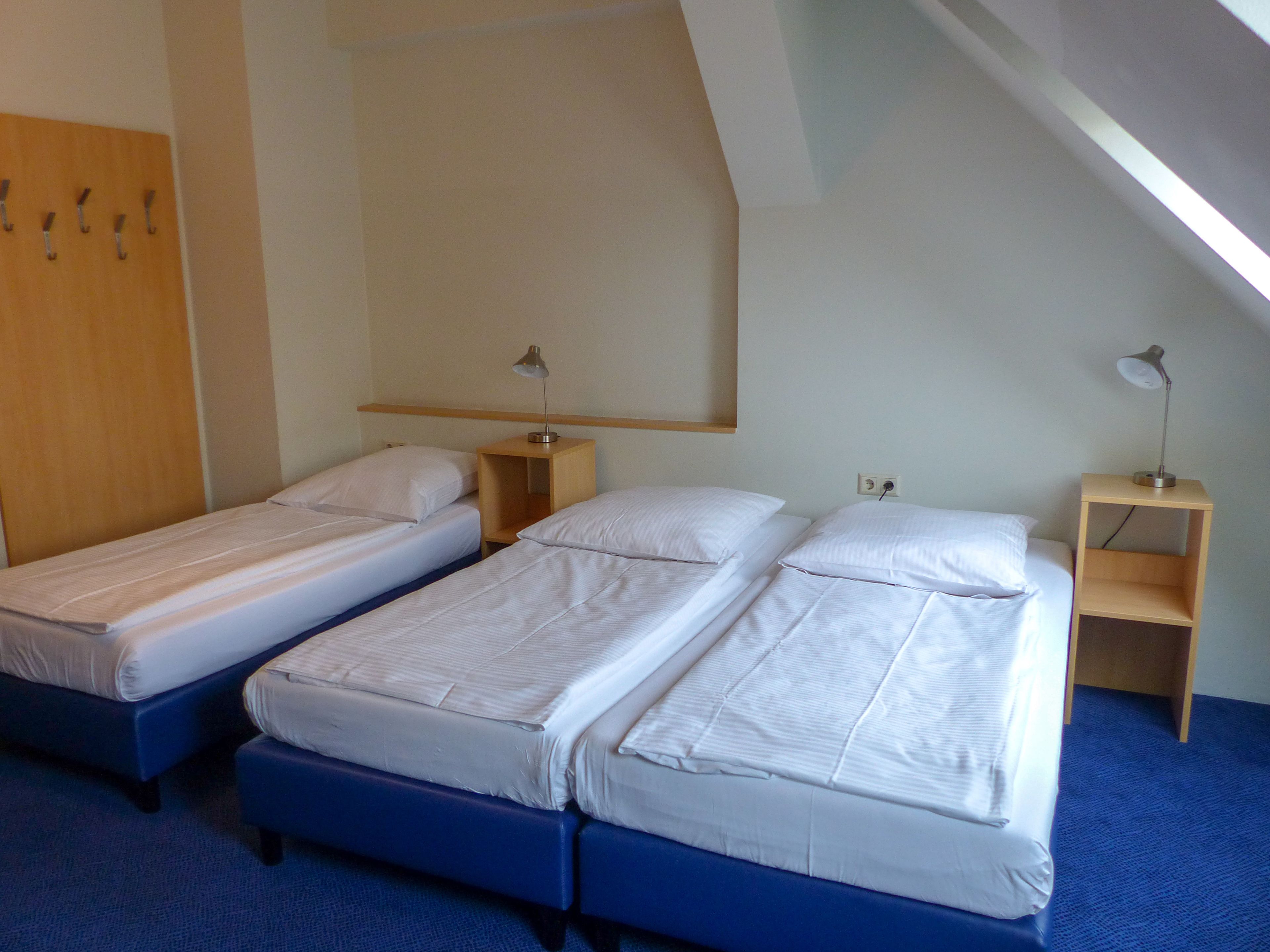 A room with two single beds, a wooden wardrobe, and a desk with a lamp.