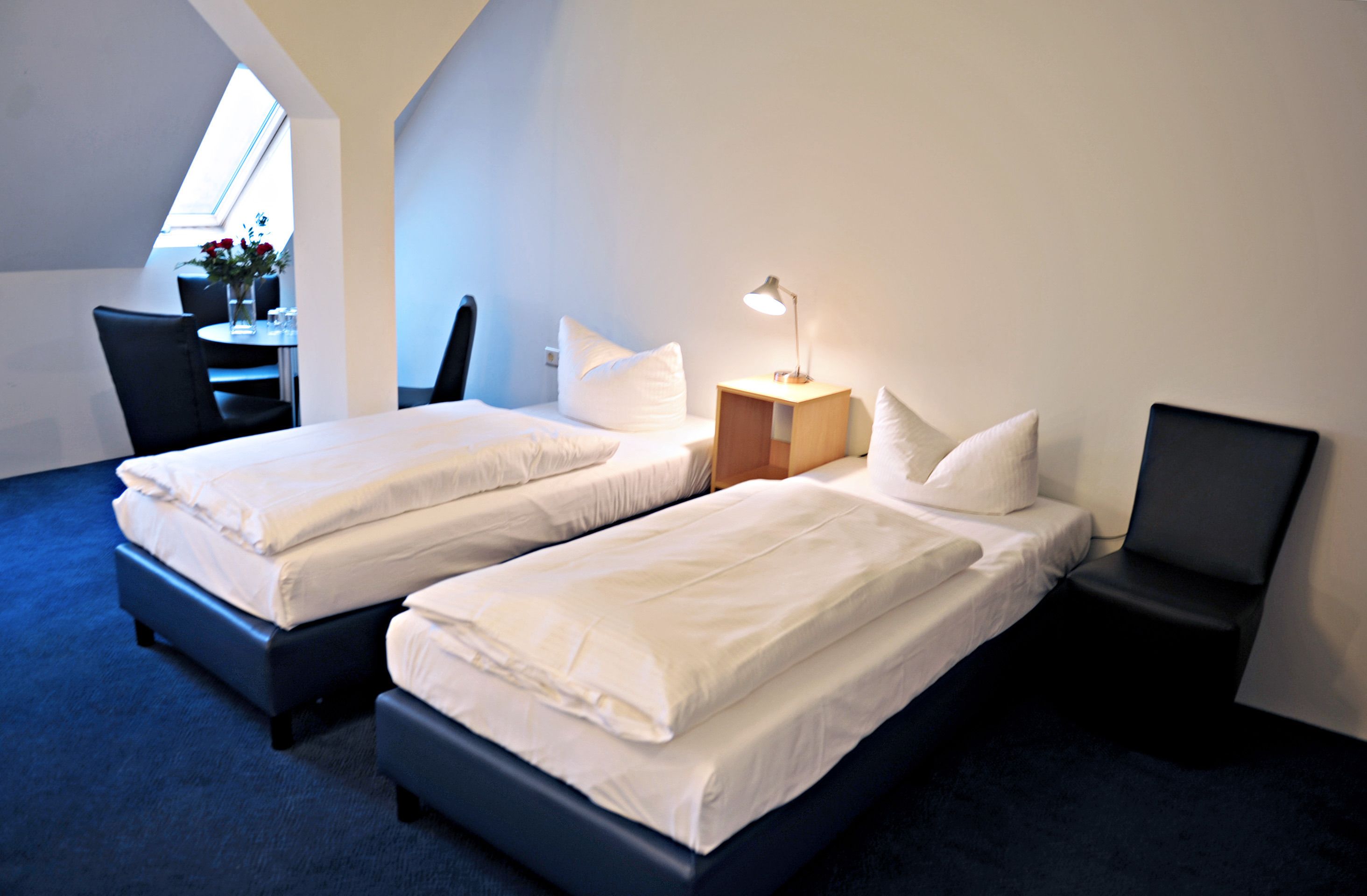 Una habitación de hotel con dos camas, un escritorio, una silla y una lámpara.