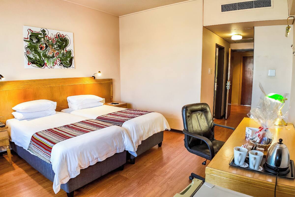 Une chambre d’hôtel avec deux lits, un bureau avec une lampe, une chaise et un tableau au mur.