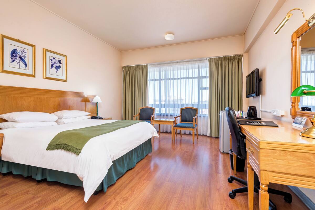 Une chambre d’hôtel équipée d’un lit, d’un bureau, de chaises, d’une télévision et d’une fenêtre avec des rideaux.