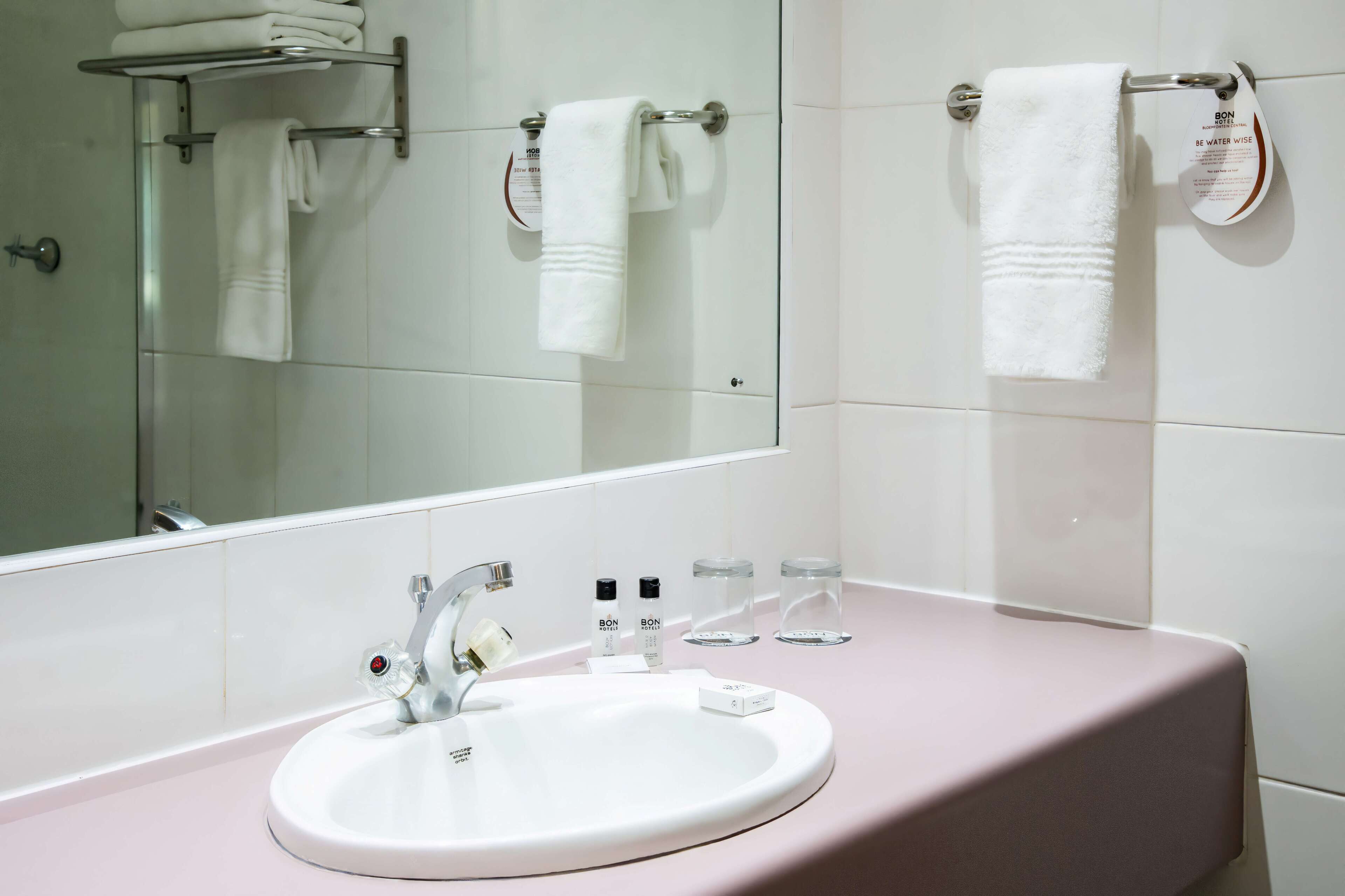 A bathroom with a white sink, a mirror, and two towels hanging on towel bars.