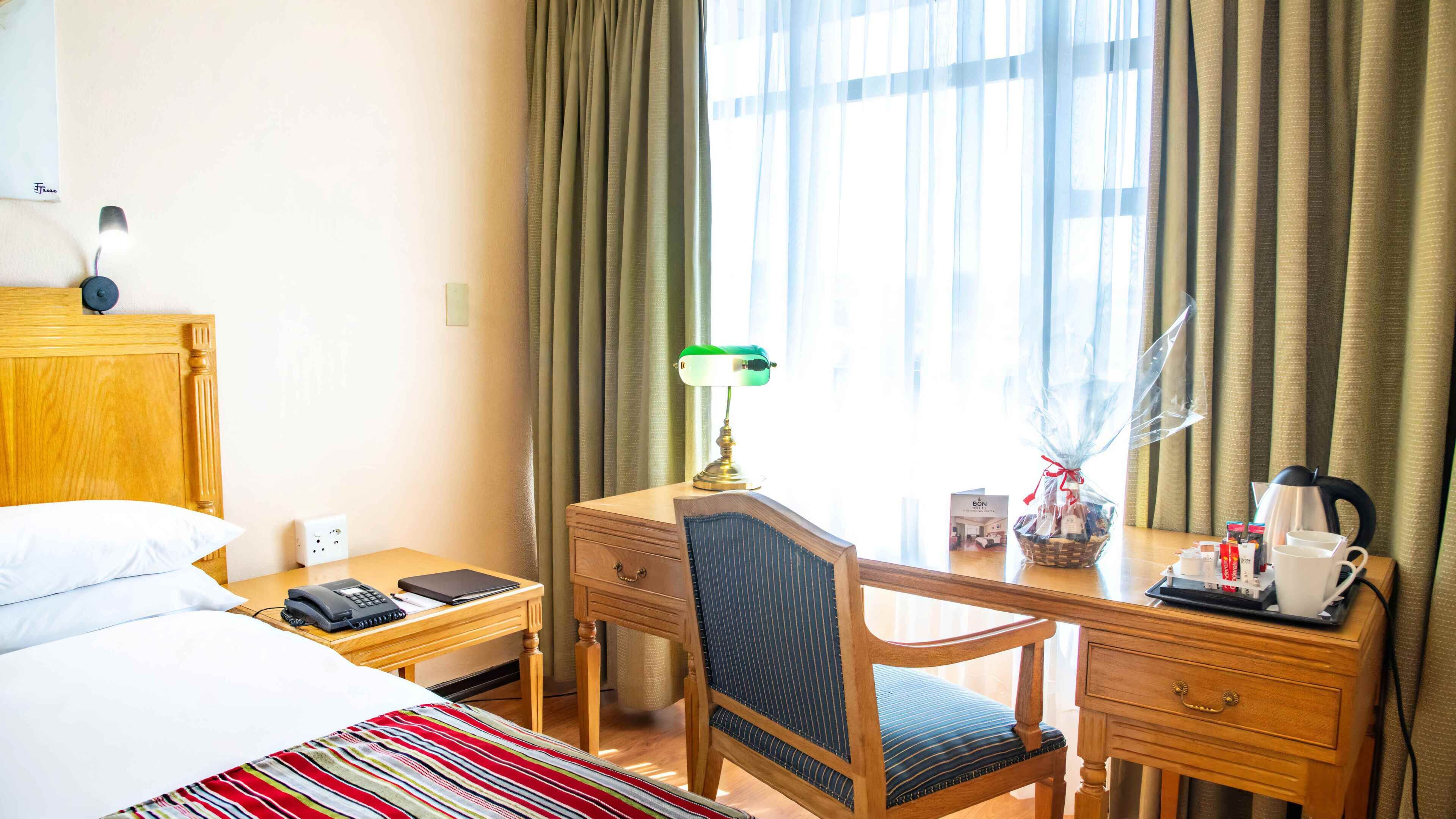 A hotel room with a bed, desk, chair, lamp, and a window with curtains.