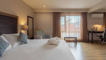 Habitación de hotel con una cama grande, un escritorio, una silla y una ventana con cortinas.