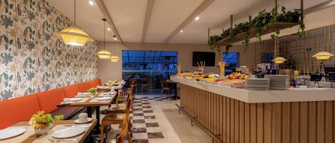 A restaurant with a checkered floor, wooden tables, orange booths, and a bar area with a fruit display.