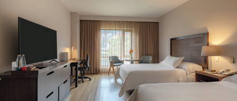 Habitación de hotel con dos camas, un escritorio con silla, televisión y minibar.