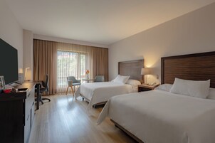 A hotel room with two beds, a desk, a chair, a TV, and a window with curtains.