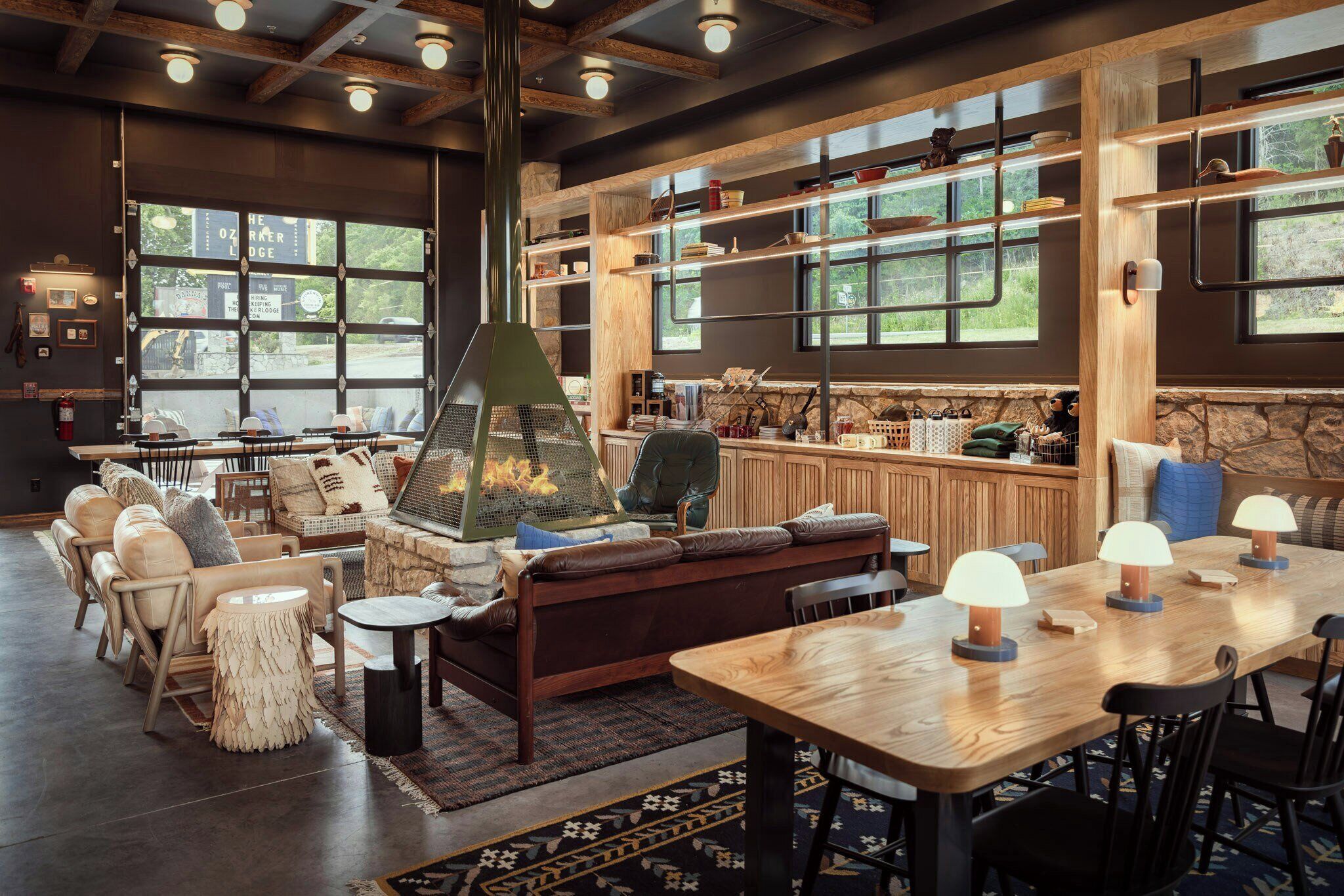 A cozy interior with a stone fireplace, wooden shelves, and a large window overlooking greenery.
