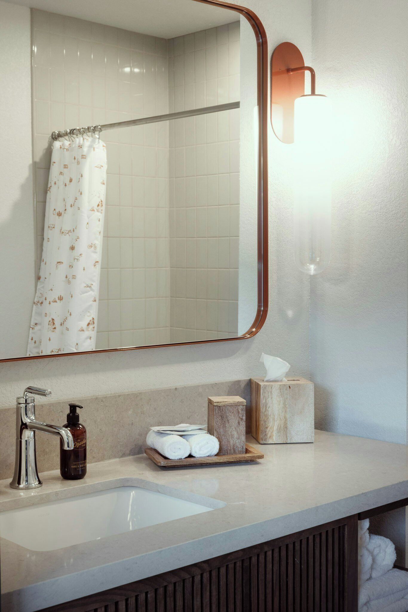 A bathroom with a white sink, a mirror with a wooden frame, a towel rack, and a bottle of soap.