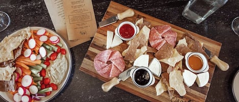 A charcuterie board with various meats, cheeses, and vegetables on a wooden board, accompanied by a menu and a glass of water.