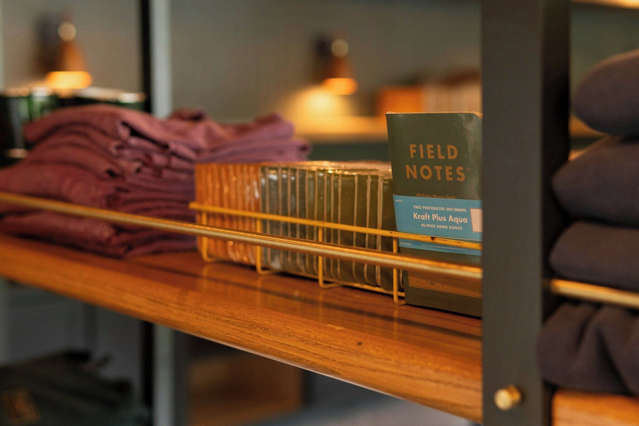 A wooden shelf with folded clothes, a metal rack, and a book titled 'FIELD NOTES.'