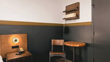 Une petite pièce, de taille modeste, comprenant une table de chevet en bois, une chaise, une petite table et une armoire.