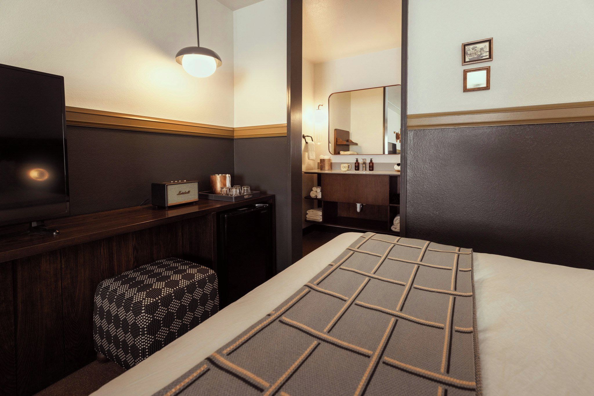 Quarto de hotel com cama, televisão, minibar e banheiro visível através de uma porta aberta.