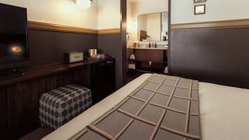A hotel room with a bed, a television, a minibar, and a bathroom visible through an open door.